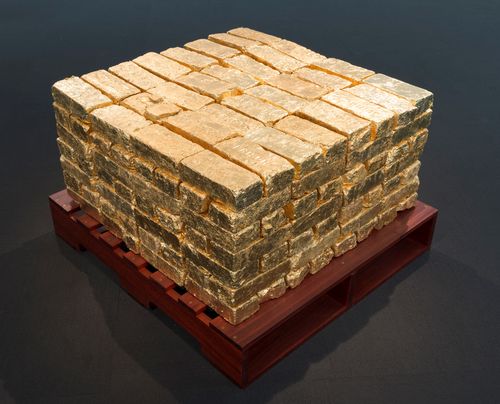 Pile of gold bricks sits atop a wooden pallet that has been painted dark red.