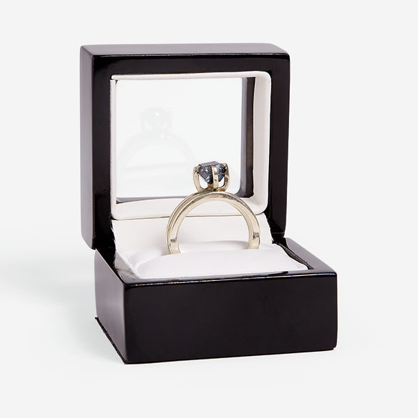 A diamond ring with a single diamond inset, standing up on an open, brown ring box, lined with white material.