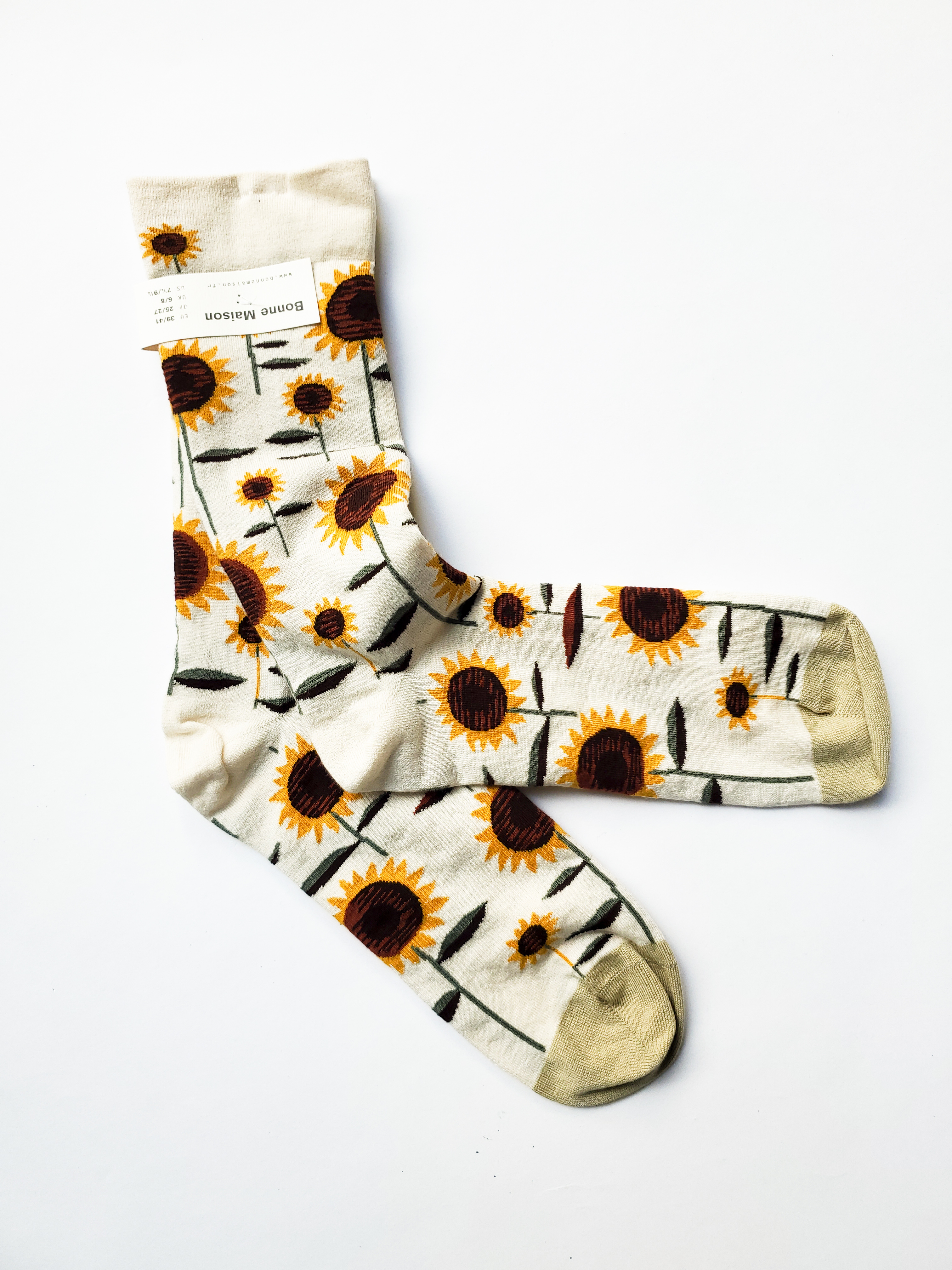 Two cream colored socks with various sized sunflower pattern on them.