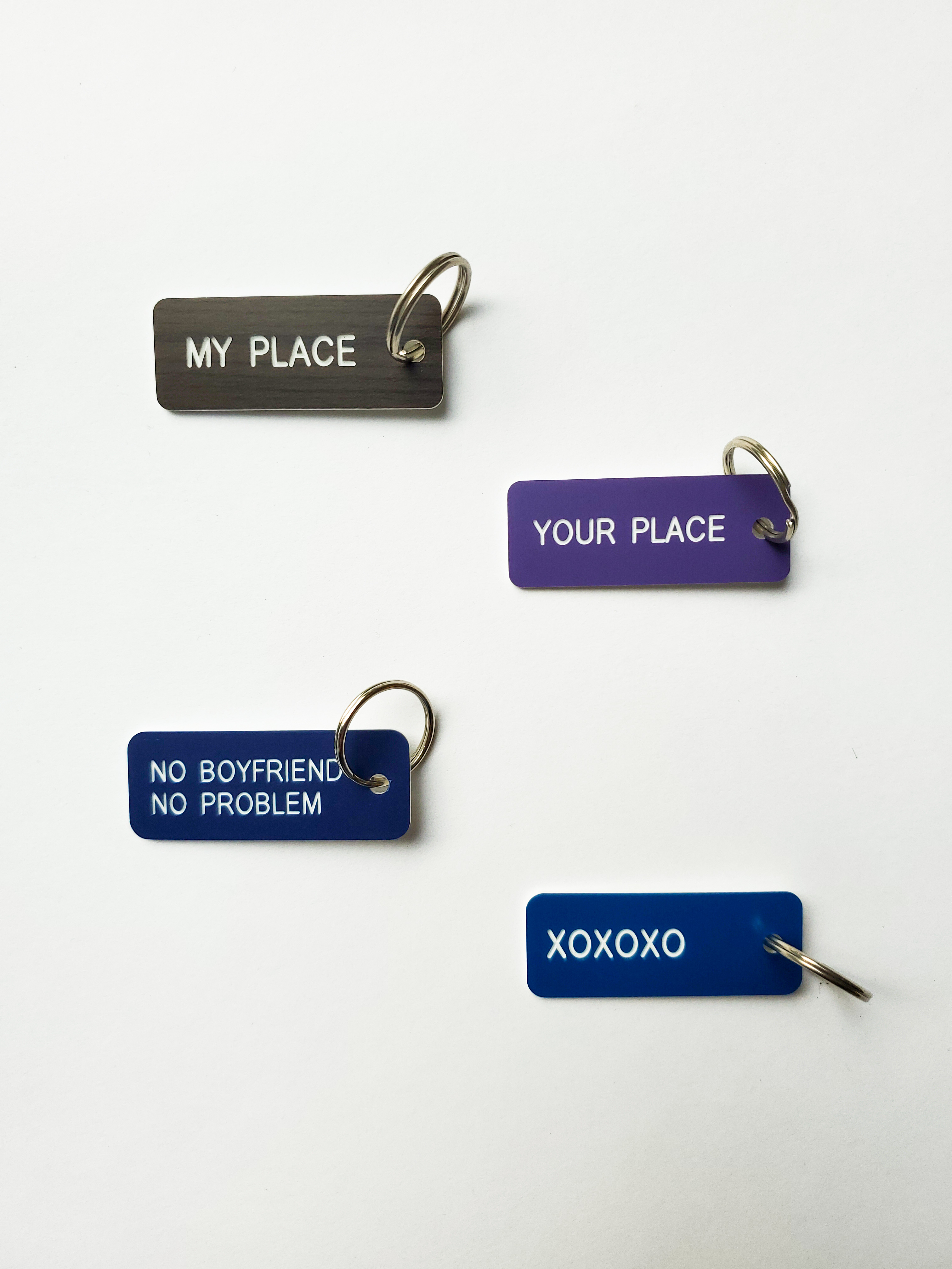Four blue metallic keytags with key rings. From top to bottom, they state "My place," "Your place," "No boyfriend no problem," "XOXOXO"