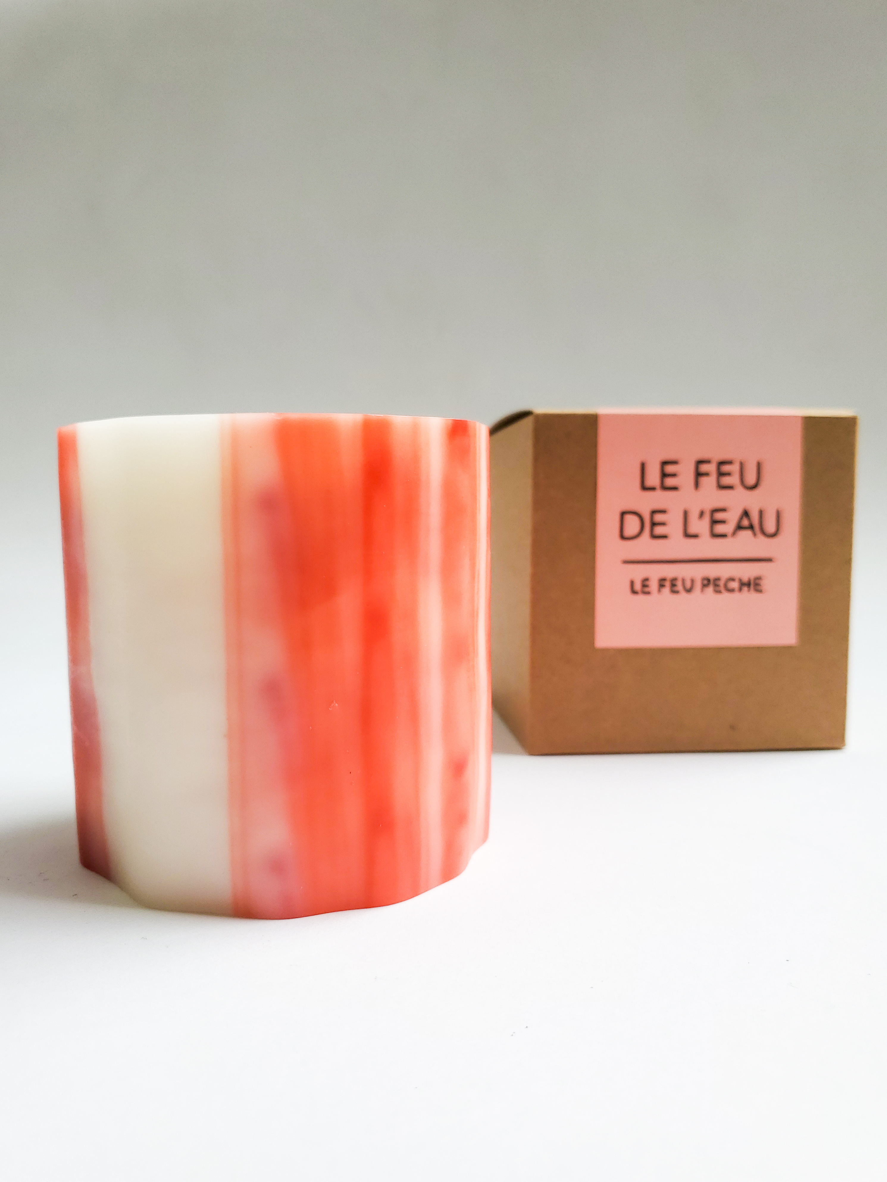 A pink candle sits next to a cardboard box that has the text "Le Feu de L'eau - Le Feu Peche" on it. 