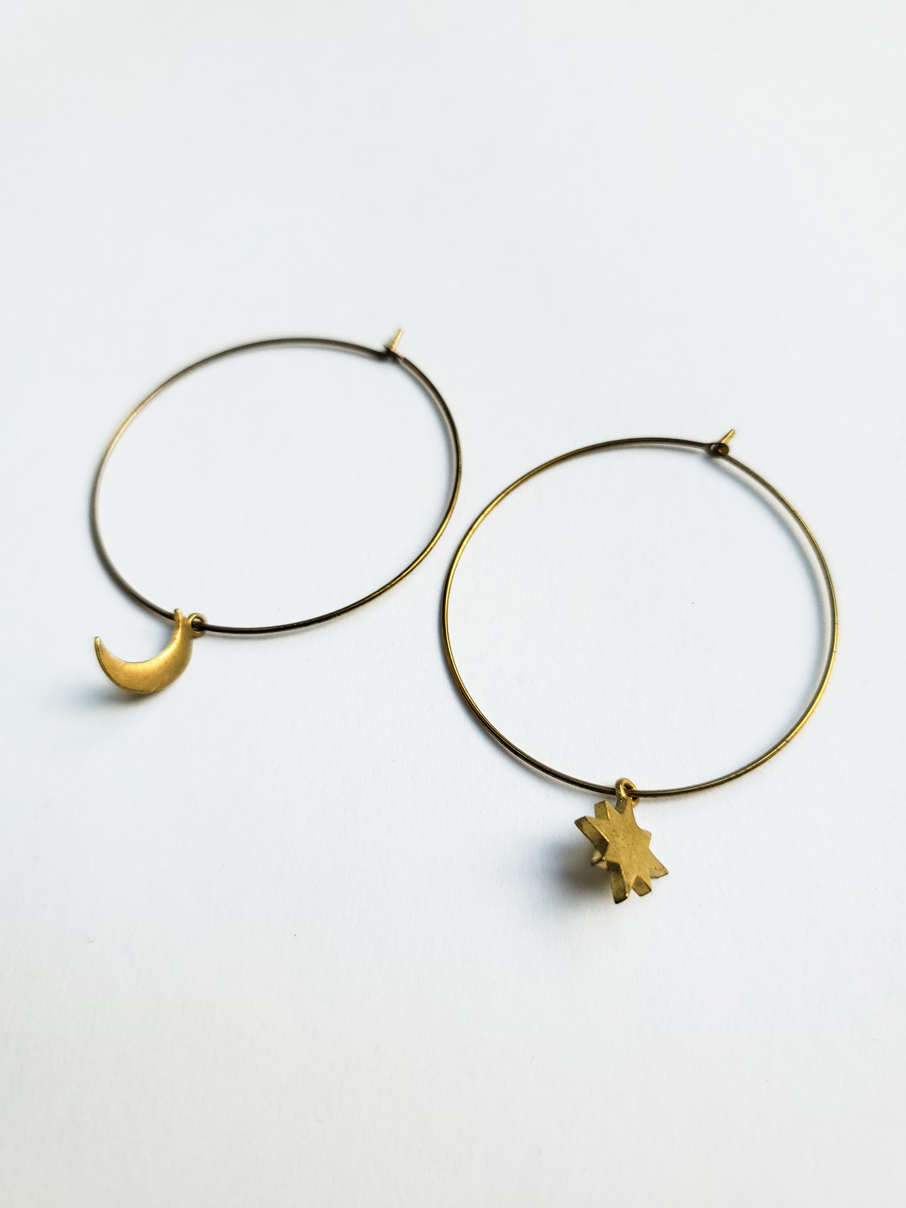 Two golden hoop earrings, one with a crescent moon charm and the other with a star charm.