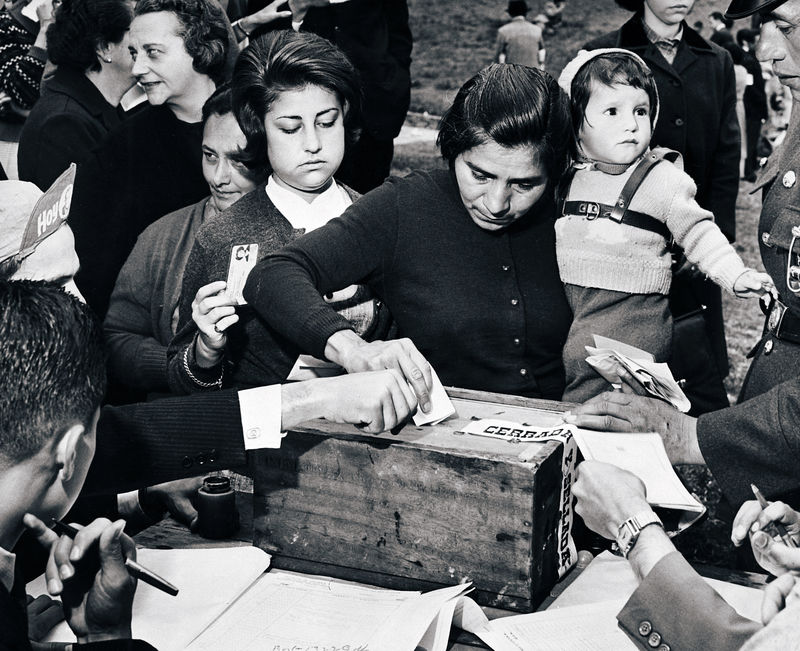 Woman carrying child deposits ballot, 1962