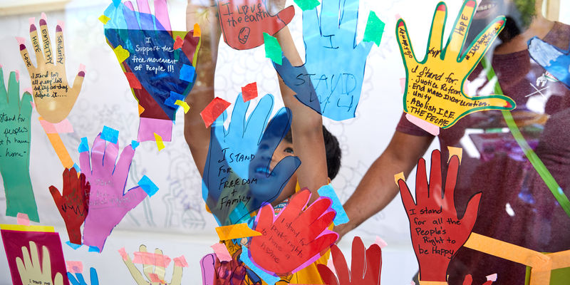 A child presses his hands to a glass covered in paper hand cut-outs