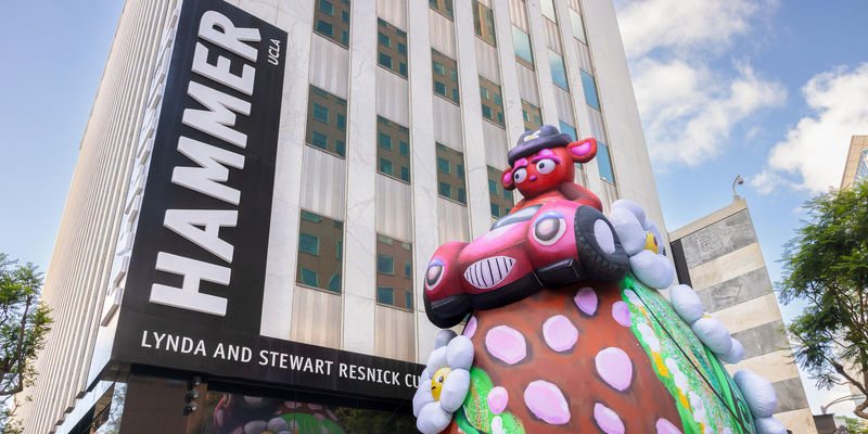 Massive outdoor inflatable portraying a stern-eyed bear in a hot-pink convertible atop a strawberry-studded shaped hilltop with daisies