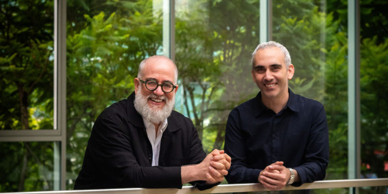 Two men leaning over a railing, smiling at the camera