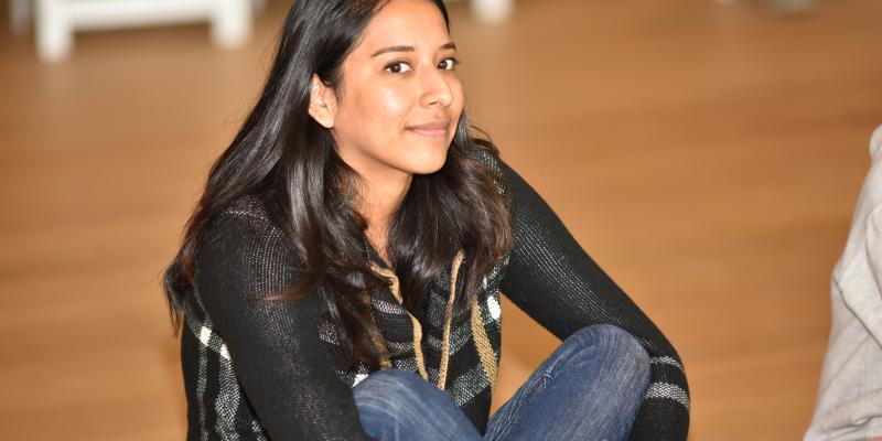Russel Altamirano smiles at the camera, siting cross-legged and  on the hardwood floor at the Hammer Museum