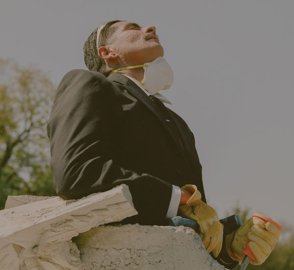 A man with a construction mask around his chin stands in a concrete tube, looking up at the sky