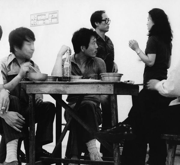 Image of men eating and drinking at a table in the middle of an art gallery