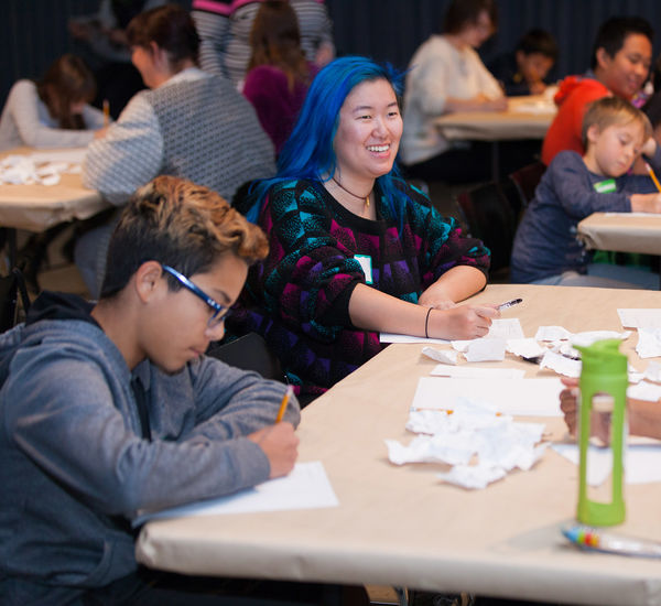 Smiling young teens sit at a table and write