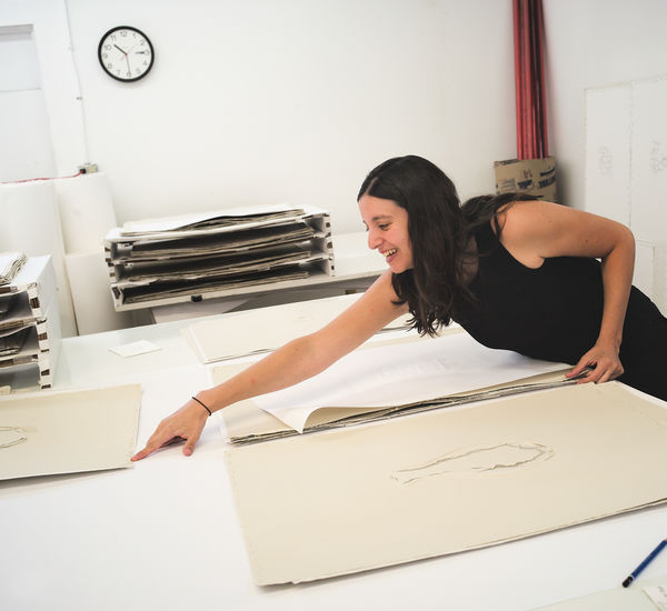 Analia Saban leans over a table to point at a print