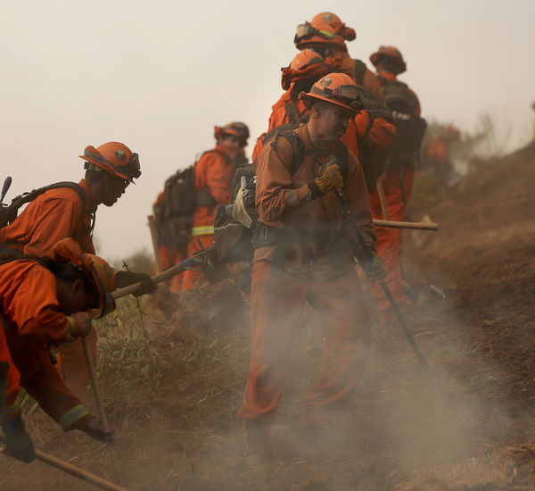 A line of inmates dressed in orange firefighting gear, digging a trench