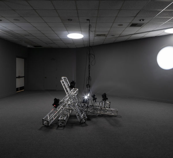 A metal installation at the center, with light and shadow in the background.