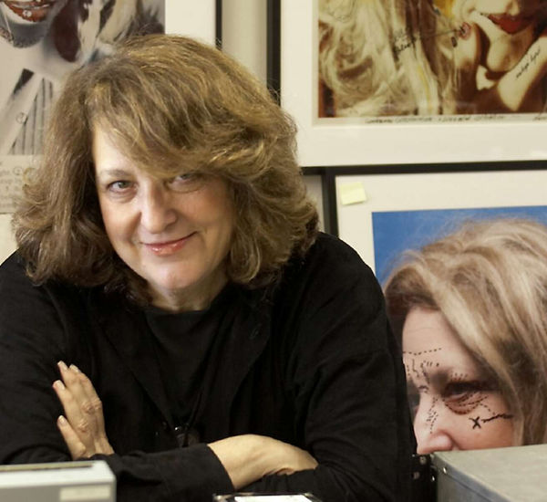 Lynn Hershman Leeson in her office with framed artwork on the walls behind her