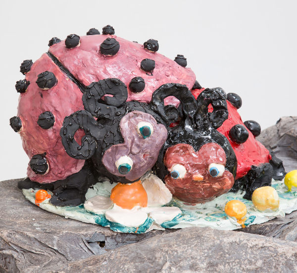 Sculpture of two ladybugs with noses and large eyes laying on top of each other
