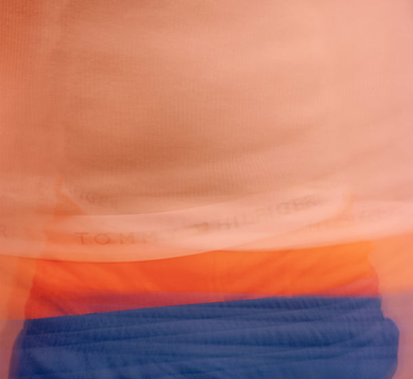 Blurred image of a torso wearing blue shorts with orange boxers peaking above the waistband, the white band of the underwear reading "TOMMY HILFIGER" in black letters