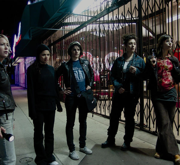 Five people stand on the sidewalk in front of a shuttered storefront