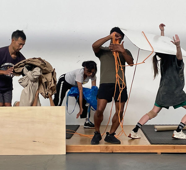 Five dancers in casual clothing interact with contsruction materials