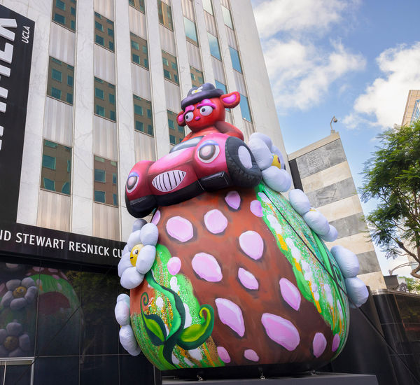 Massive outdoor inflatable portraying a stern-eyed bear in a hot-pink convertible atop a strawberry-studded shaped hilltop with daisies
