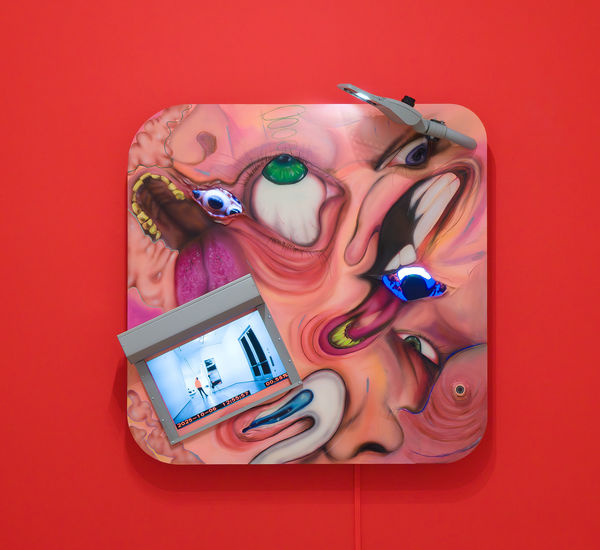 Square multi-media work with distorted images of faces and video screens, on a bright red wall