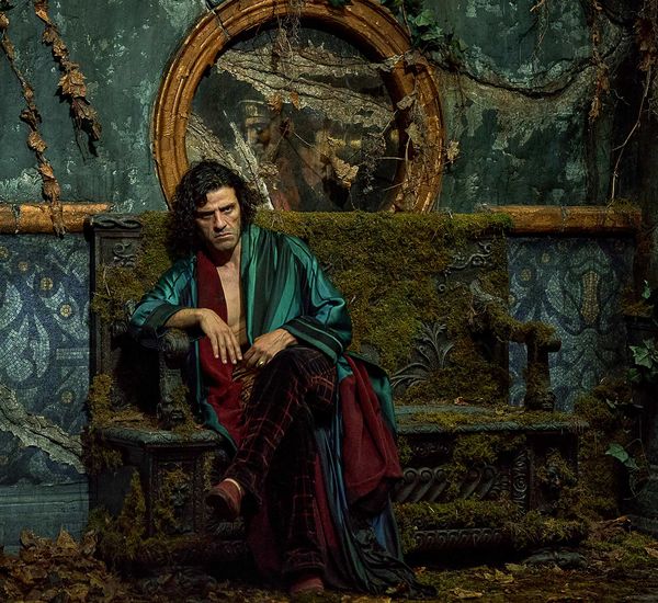 Oscar Isaac as Dr. Frankenstein, dressed in lush robes, sits pensively on a bench overgrown with weeds