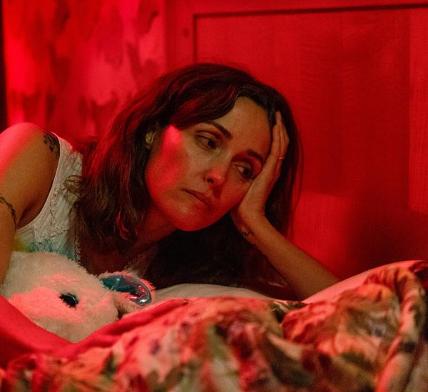 Rose Byrne lays in a bed holding a stuffed animal