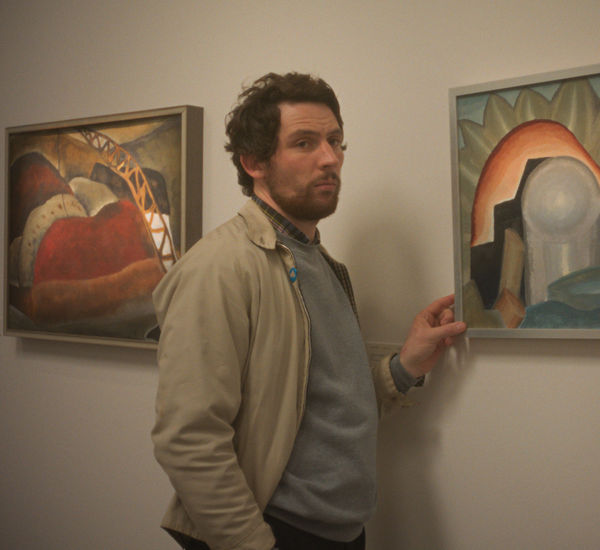 A man in a tan jacket fingers a framed painting