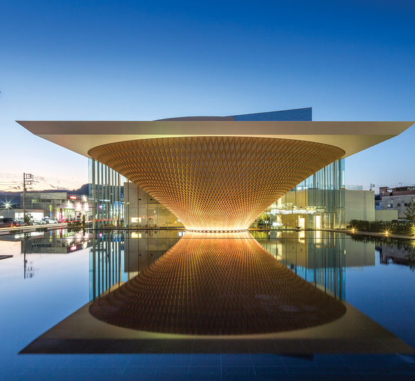 A glowing building in the shape of an inverted pyramid, with a reflecting pool in front of it