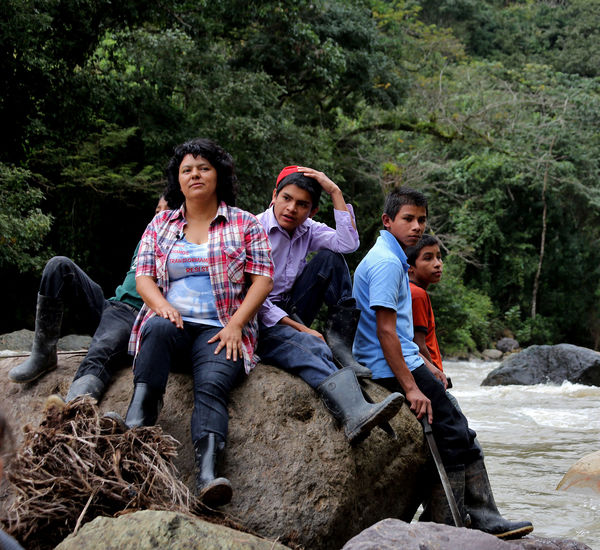 Berta Cáceres and four young men sit on a boulder in a river