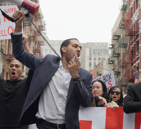 A man with a loudspeaker stands at the front of a large protest