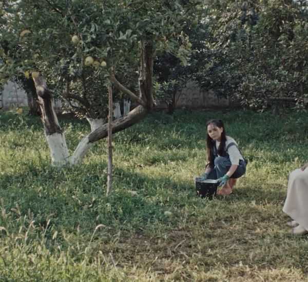 A girl kneels next to a woman in all white amidst a garden