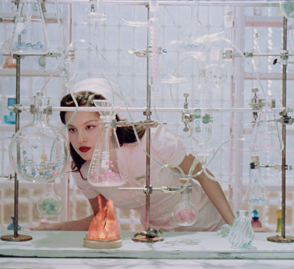 Olivia Rodrigo looks intently at a glass beaker while wearing a vintage nurse outfit