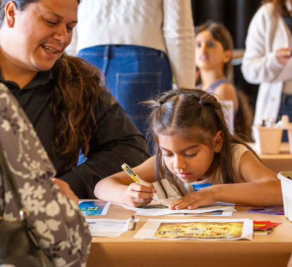 Child draws at a table while adults look on