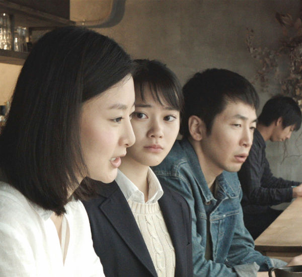 Two women and a man, viewed in profile, sit at a bar counter