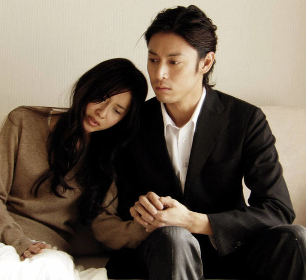 A mand and woman sit on a couch holding hands