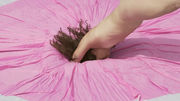A stretched-out, naked figure appears to dive from the upper right corner into  the center of a round pink  textile.