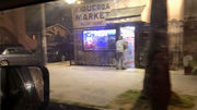 Video taken from a moving car while passing a corner store with sign reading "FIGUEROA MARKET," neon lights glowing from inside the building