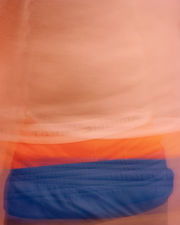 Blurred image of a torso wearing blue shorts with orange boxers peaking above the waistband, the white band of the underwear reading "TOMMY HILFIGER" in black letters