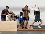 Five dancers in casual clothing interact with contsruction materials