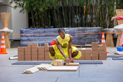 A dancer in a yellow outfit smiles as he kneels in front a stack of wood pieces