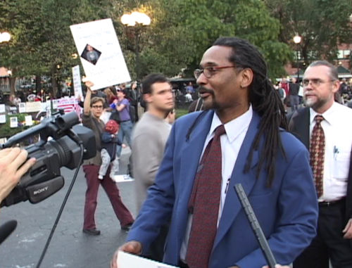 A man in a suit and tie stands before a camera in a crowd