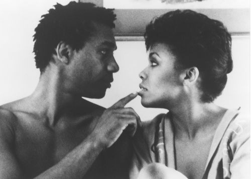 Still from the film The Brother From Another Planet (1984) showing a close-up of a shirtless man looking into the eyes of a woman in a robe and touching her lip