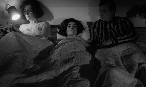 Still from the film Duet for Cannibals (1969) showing two women and a man in bed.