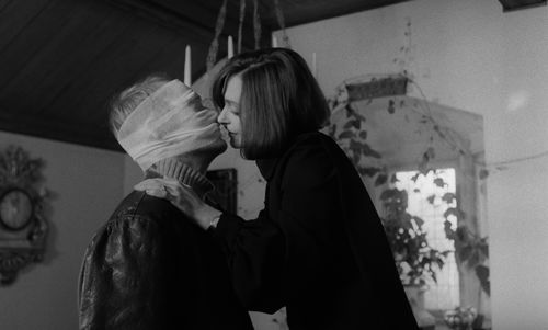 Still from the film Duet for Cannibals (1969) showing a woman leaning in to kiss a person whose face is covered in bandages.