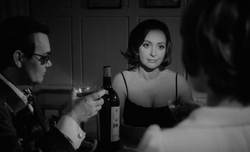 Still from the film Duet for Cannibals (1969) showing a woman staring intensely at another woman in the foreground while a man watches