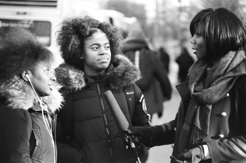 Two teenage girls stand before a woman with a microphone