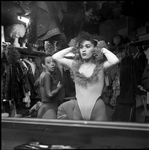 Two figures stand before a dressing room mirror