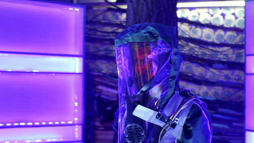 A man in a haz-mat suit stands in a purple room