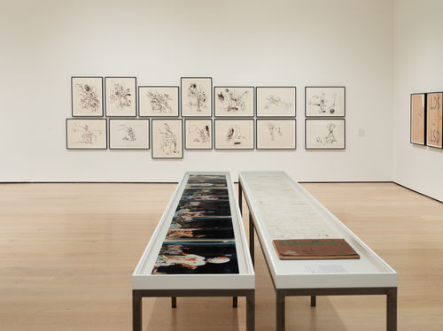 Two display tables before a wall of sketches