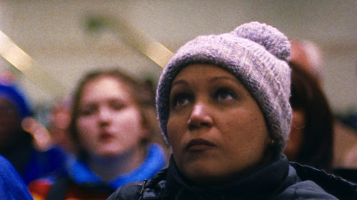 A woman in a purple knit cap looks up from a crowd